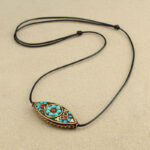 Tibetan turquoise marquise pendant necklace with ethnic red enamel inlay and black waxed cord, flat lay top view