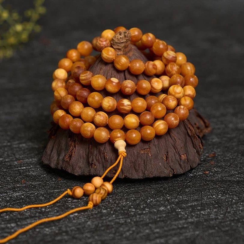 stacked 108-bead mala necklace showing dense amber-toned wooden beads and hanging decorative tassel detail close-up