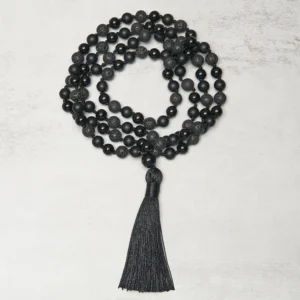 Flat lay centered composition of coiled 8mm black bead tibetan prayer necklace with tassel on light background