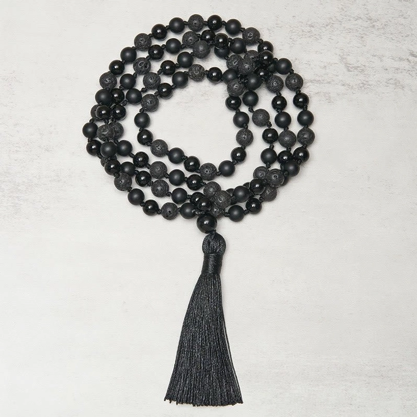 Flat lay centered composition of coiled 8mm black bead tibetan prayer necklace with tassel on light background