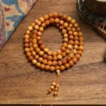 108 pine wood prayer beads mala necklace with amber-brown wooden beads and decorative tassel on ethnic fabric background