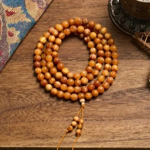 108 pine wood prayer beads mala necklace with amber-brown wooden beads and decorative tassel on ethnic fabric background