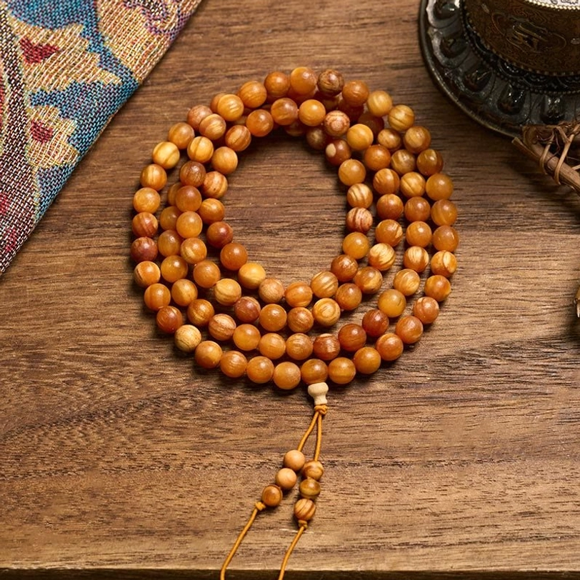 108 pine wood prayer beads mala necklace with amber-brown wooden beads and decorative tassel on ethnic fabric background
