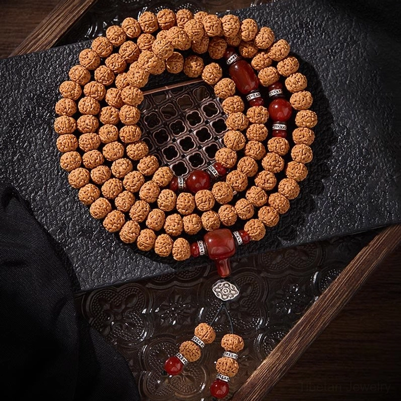Bodhi seed mala prayer necklace laid on grid mat with glass tray, showing light brown textured beads with red agate spacers and silver accents