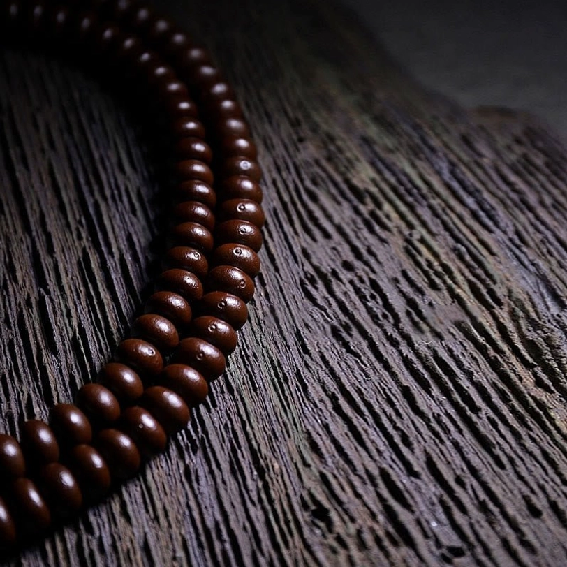 Uniform purple bodhi seed beads in 108-bead mala configuration on textured wooden surface