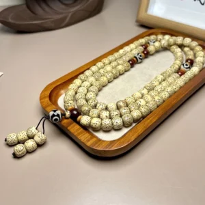 Flat lay view of 108 Bodhi seed mala beads with protective Dzi bead arranged neatly on wooden tray background