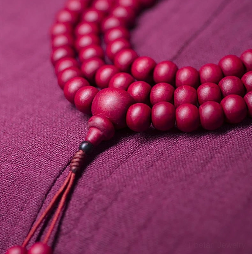 Flat lay of complete 108 bead mala bracelet showing natural wood grain texture on red abelia biflora beads with counter bead and double red tassels