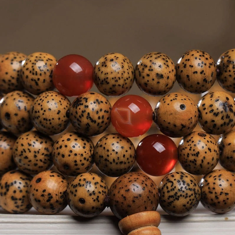 Direct overhead flat lay of mala beads highlighting large red agate stones, textured spotted bodhi seeds, and wooden counter beads