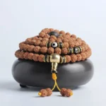 108 mala bracelet with rudraksha beads, bodhi seeds, and black dzi bead accents displayed on ceramic holder - front overhead view