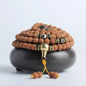 108 mala bracelet with rudraksha beads, bodhi seeds, and black dzi bead accents displayed on ceramic holder - front overhead view