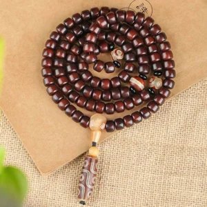 Coiled 108 mala bead necklace with dzi bead pendant in reddish-brown tones on linen fabric background