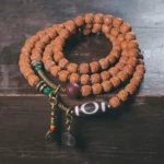 108 Rudraksha Mala Bracelet with Nine-Eye Dzi Bead displayed on dark wooden surface, showing complete design with tassel and multi-loop arrangement