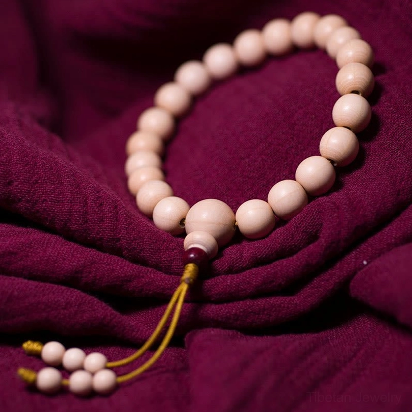 Full flat lay view of 21-bead Abelia Biflora wood wrist mala bracelet displaying neat arrangement of cream beads with matching yellow tassel decoration on dark cloth