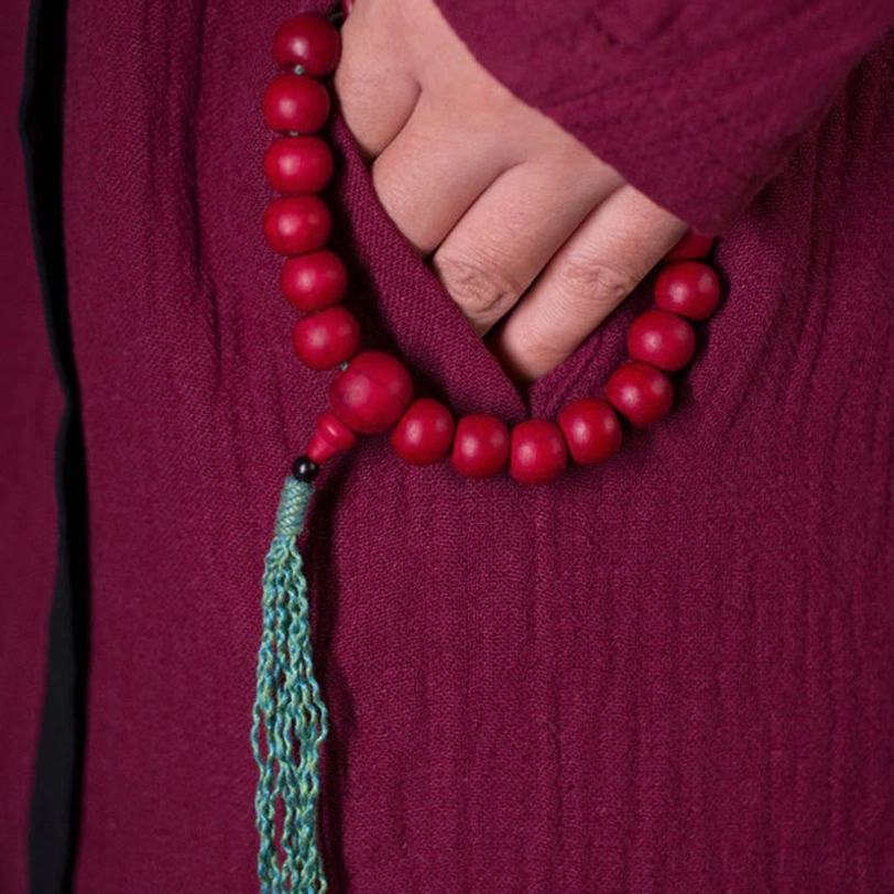 Wrist mala bracelet worn under maroon sleeve showing red beads and teal tassel styling