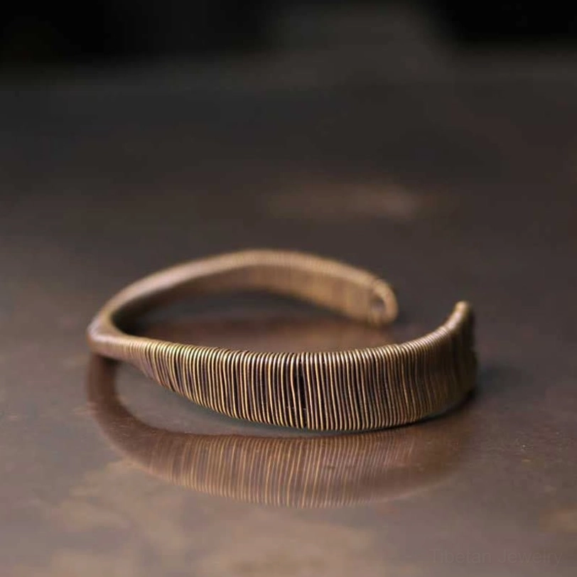 Brass cuff bracelet in vintage bronze tone captured from three-quarter angle on reflective wooden table background