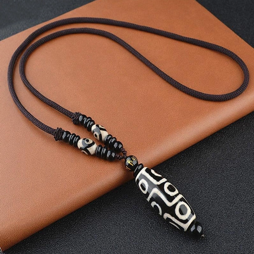 Adjustable black nine-eye Dzi bead necklace with long woven cord displayed on brown leather mat, Tibetan spiritual protection amulet