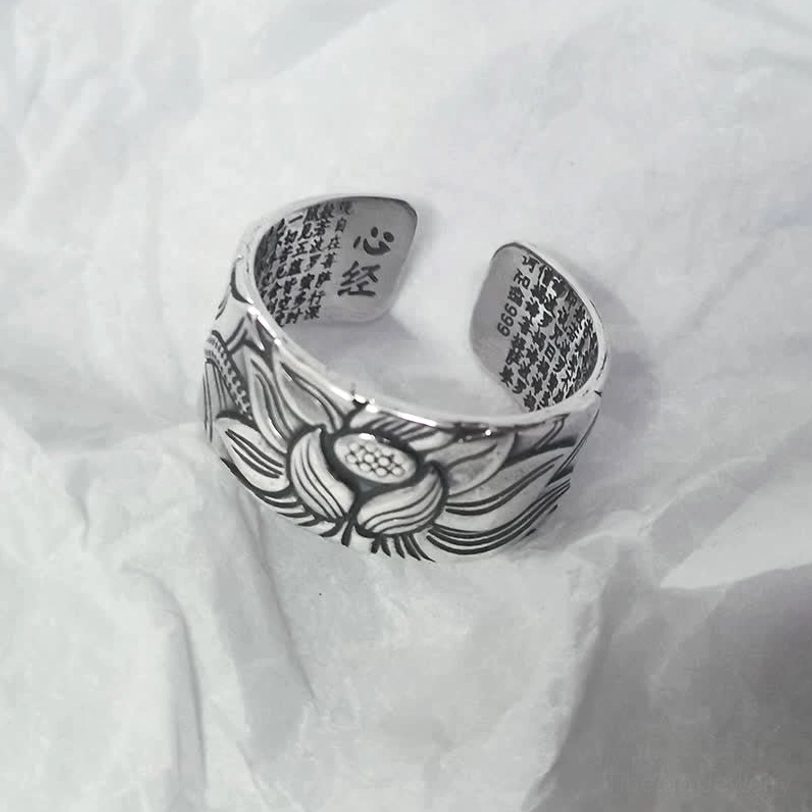 Silver lotus protection ring with heart sutra text printed on inner surface, oblique side view on white crumpled fabric background