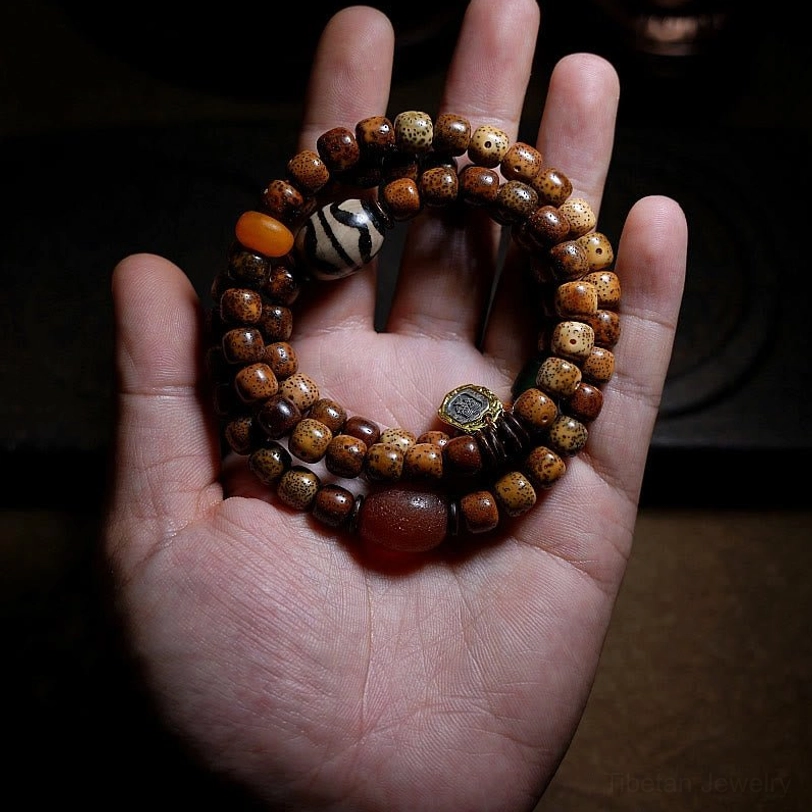 Loose reddish-brown round agate beads displayed with aged bodhi seed bracelet section on dark textured stone surface