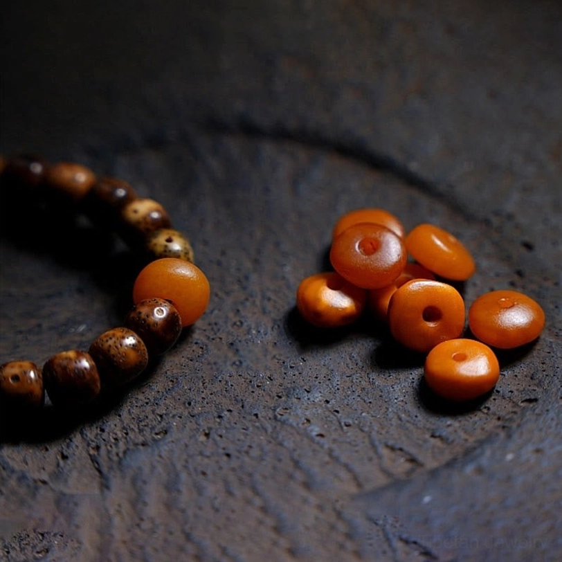 Smooth orange amber beads scattered with aged brown bodhi seed bracelet section on dark textured stone surface