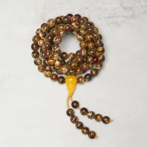 Close-up view of coiled amber mala showing intricate bead details and dangling tassel with guru bead close-up