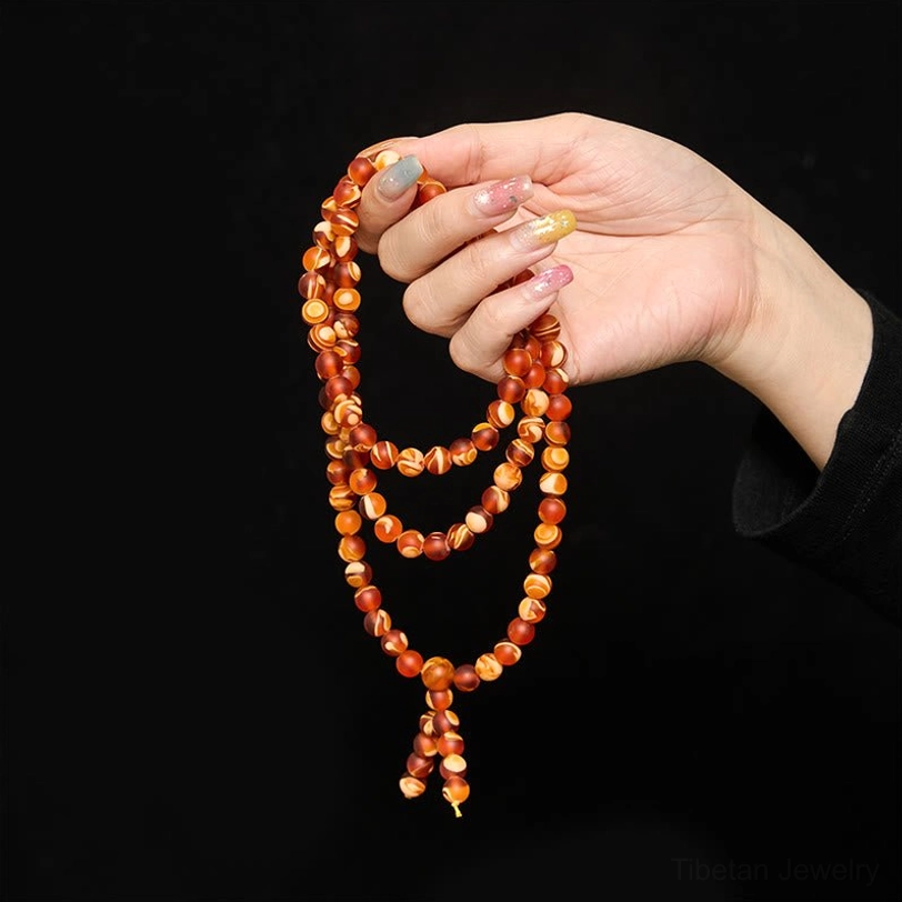 Close-up of amber prayer mala held in fingers against black background, showing three-strand layout and bead arrangement