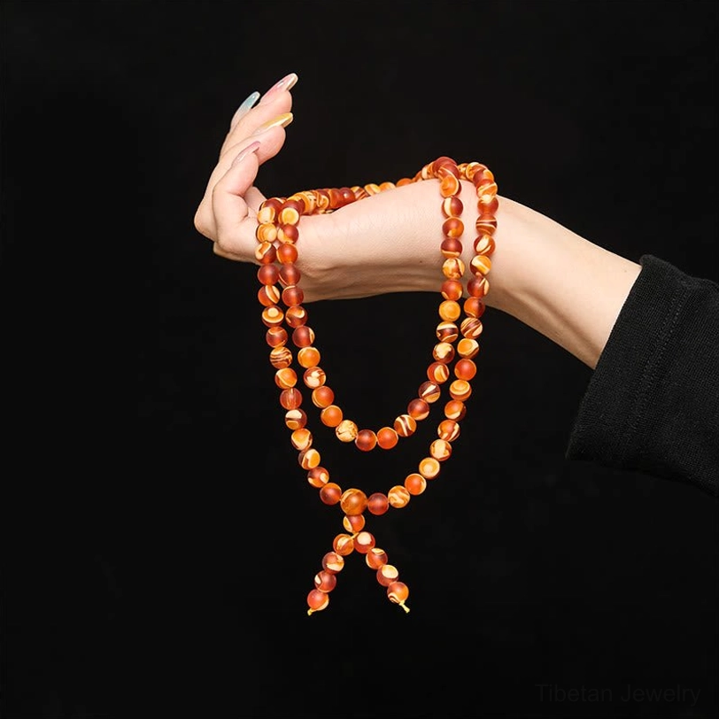 Amber mala bracelet worn on human hand against black background, displaying double-strand design and wearable length