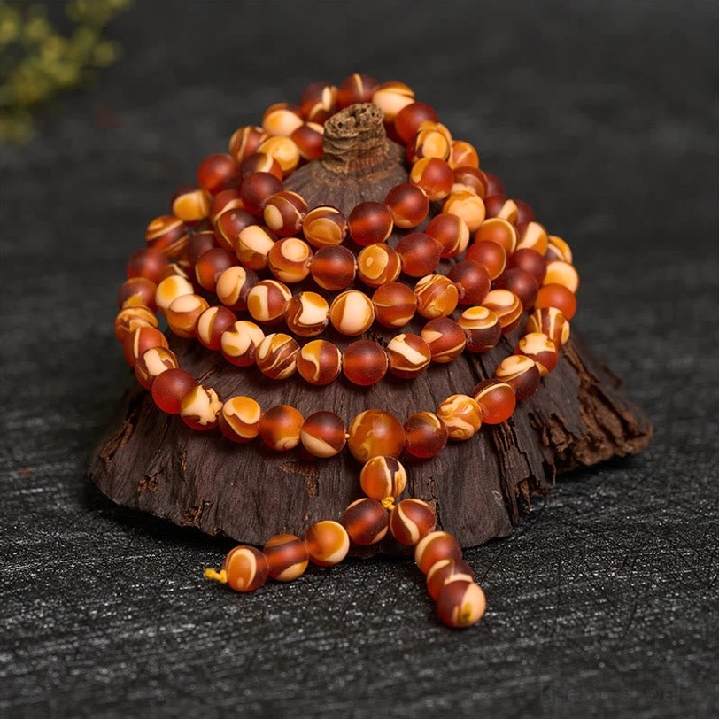 Close-up overhead view of stacked amber mala beads on dark stone with wooden display stand, showing two-tone bead texture and tassel detail