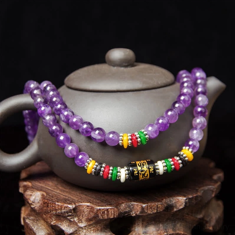 Amethyst beaded prayer string with mantra accessories displayed on purple teapot and wooden stand