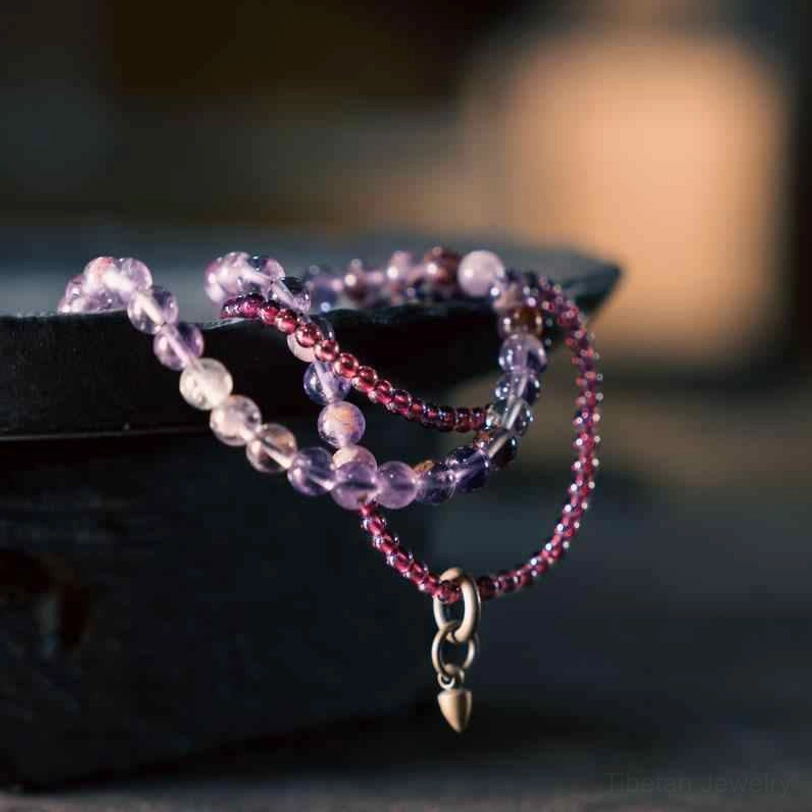 Amethyst and garnet multilayer healing bracelet with brass pendant, side view on dark tray