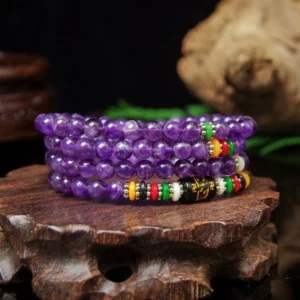 Purple amethyst prayer mala beads with six-word mantra decorations arranged on wooden base with green plants