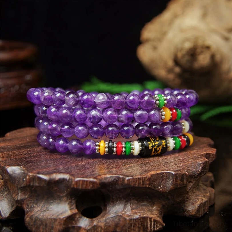 Purple amethyst prayer mala beads with six-word mantra decorations arranged on wooden base with green plants