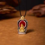 Tibetan Avalokitesvara copper dzi pendant necklace front view with gilt Buddha carving on wooden surface