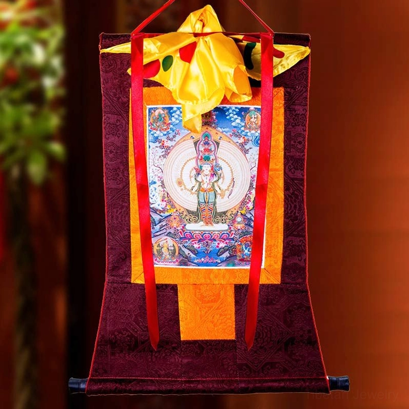 Thousand-armed Avalokitesvara thangka close-up frontal view with yellow satin panel top cover and red hanging cords against foliage background