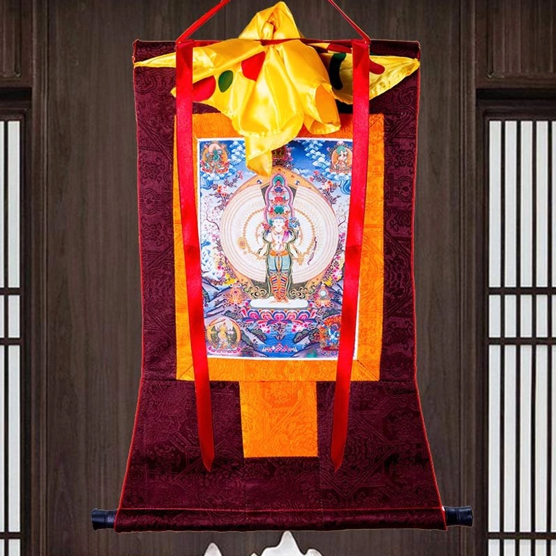 Tibetan thousand-armed Avalokitesvara thangka wall art with dark red brocade frame, red hanging ribbons and yellow top cover near wooden window