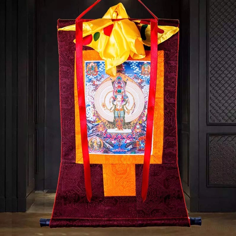 Sacred Tibetan Buddhist thangka with embossed dark red fabric frame and red hanging cords displayed against wooden door background