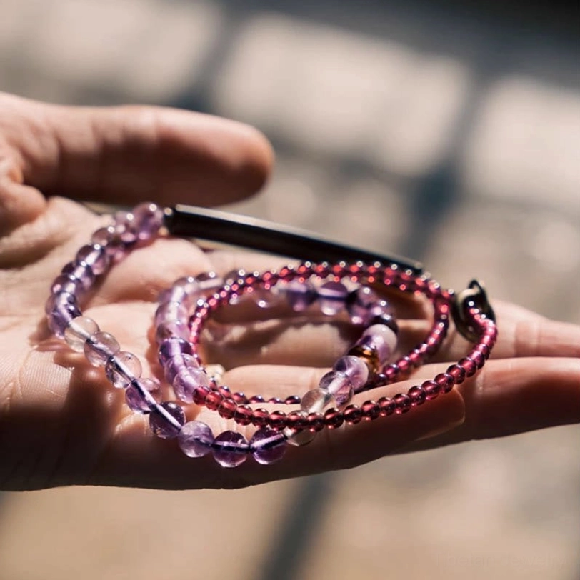 Amethyst and garnet healing bracelet held in hand with metal clasp visible outdoors