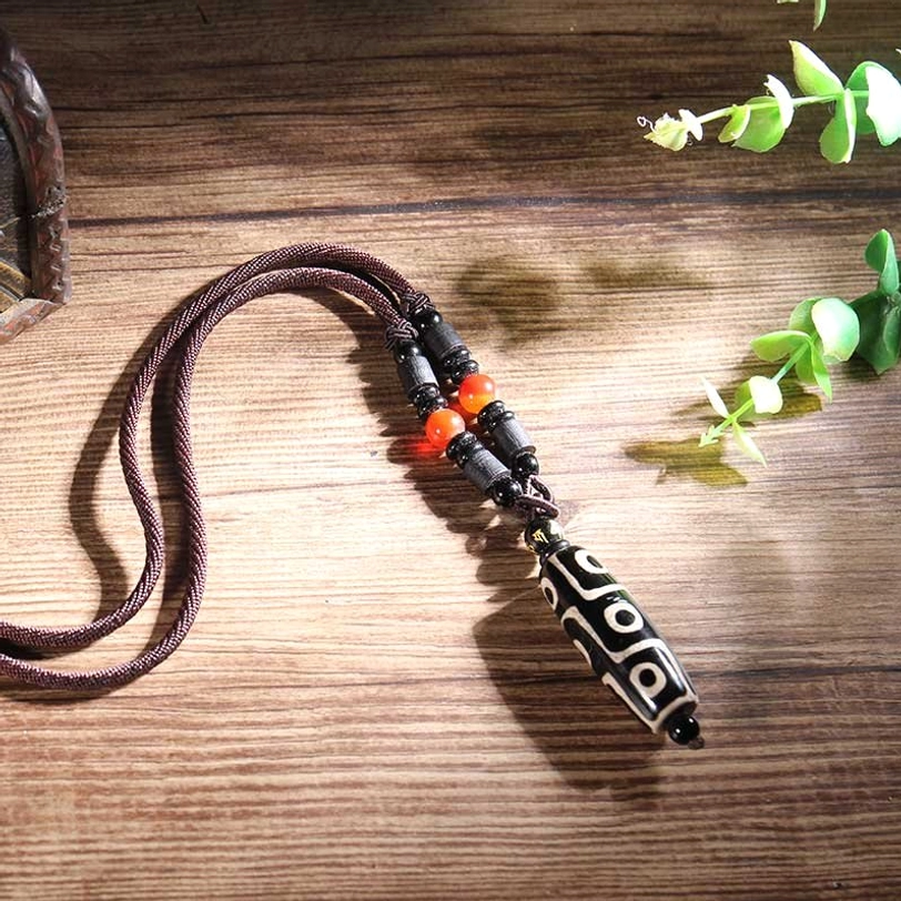 Black nine-eye dzi bead necklace flat lay with brown rope and red agate spacer beads