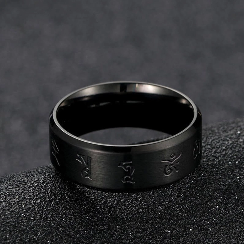 Black Jambhala mantra titanium steel ring top-down side view on dark fabric background, displaying matte black finish with engraved Buddhist mantras