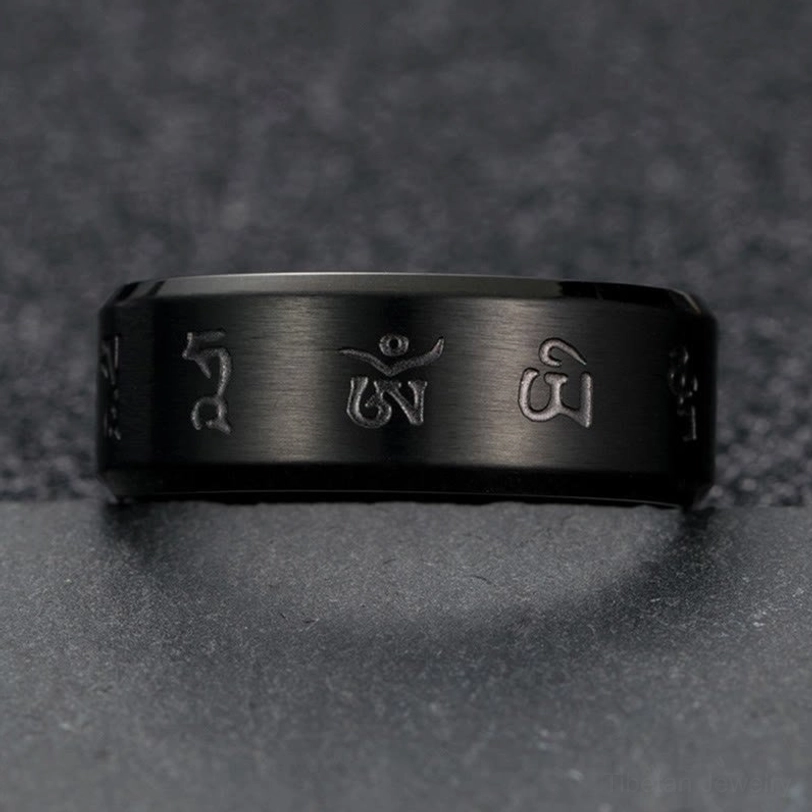 Black Jambhala Mantra ring flat lay front view on dark granular background, clearly showing three engraved Sanskrit mantras on ring face