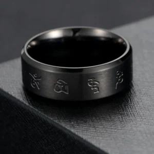 Black Jambhala mantra titanium steel ring top-down side view on dark stone platform, displaying polished and brushed surface details with engraved Buddhist mantras