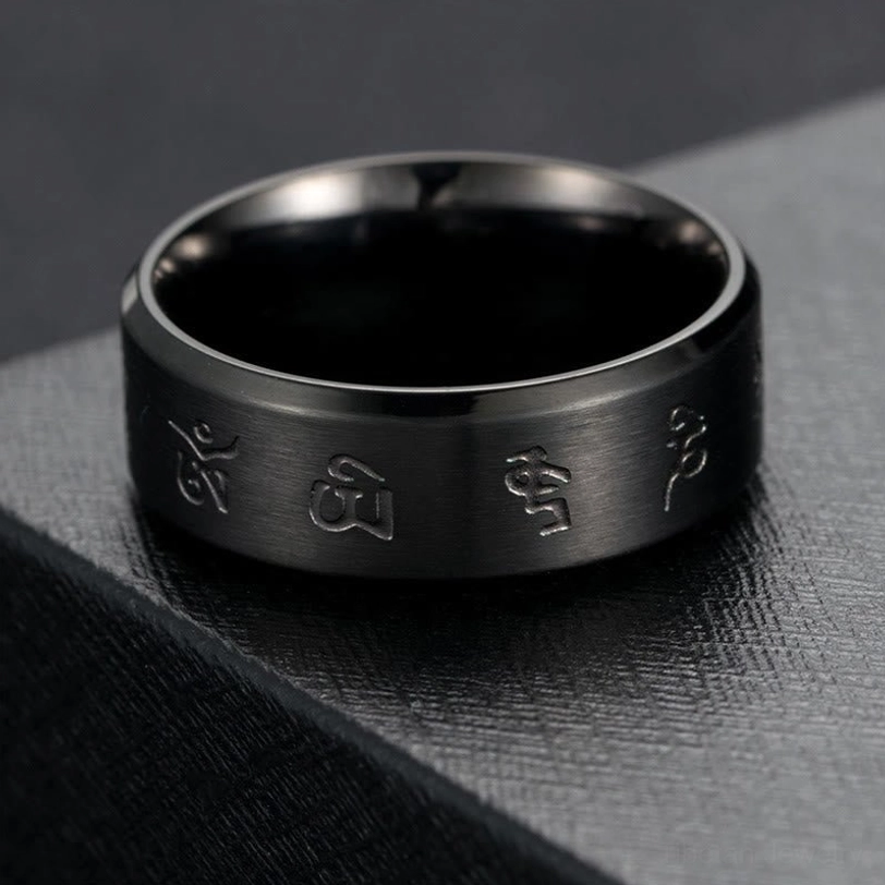 Black Jambhala mantra titanium steel ring top-down side view on dark stone platform, displaying polished and brushed surface details with engraved Buddhist mantras