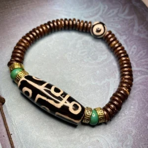 Black nine-eye dzi bead bracelet with white eye pattern, turquoise spacer, and brown agate disc beads on light purple textured background