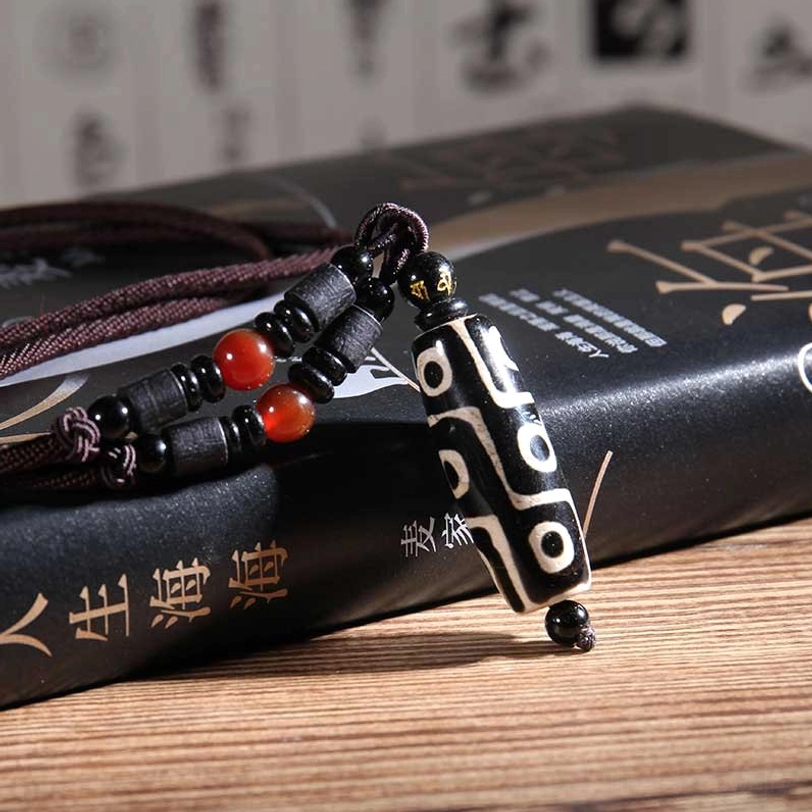 Black nine-eye dzi bead pendant closeup showing etched design with black beads and red agate accents