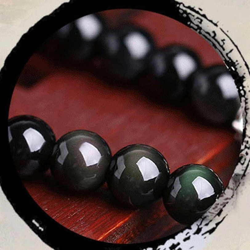 Black obsidian bead macro shot showing iridescent green cat-eye effect and deep black color
