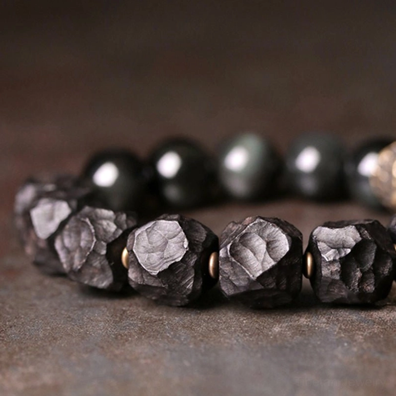 Macro close-up of rough carved black obsidian beads with copper spacer accents on dark surface