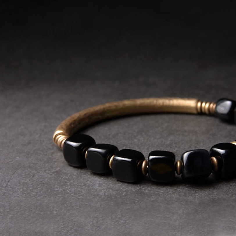 Arranged black obsidian beads and brass end caps in oblique top-down view on gray background, composition detail