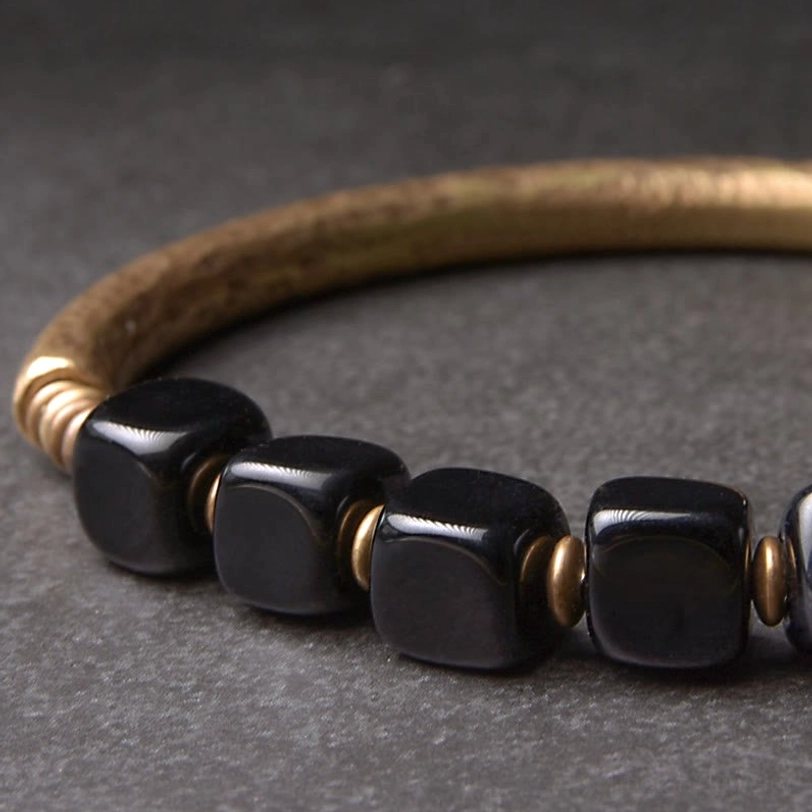 Extreme close-up of polished black obsidian cube beads and brass spacer rings on gray background, detail shot