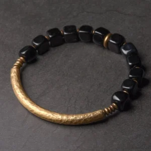 Black obsidian and brass couple bracelet flat lay overhead view on gray background, showing polished stone beads and hammered metal accents