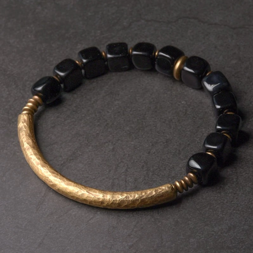 Black obsidian and brass couple bracelet flat lay overhead view on gray background, showing polished stone beads and hammered metal accents