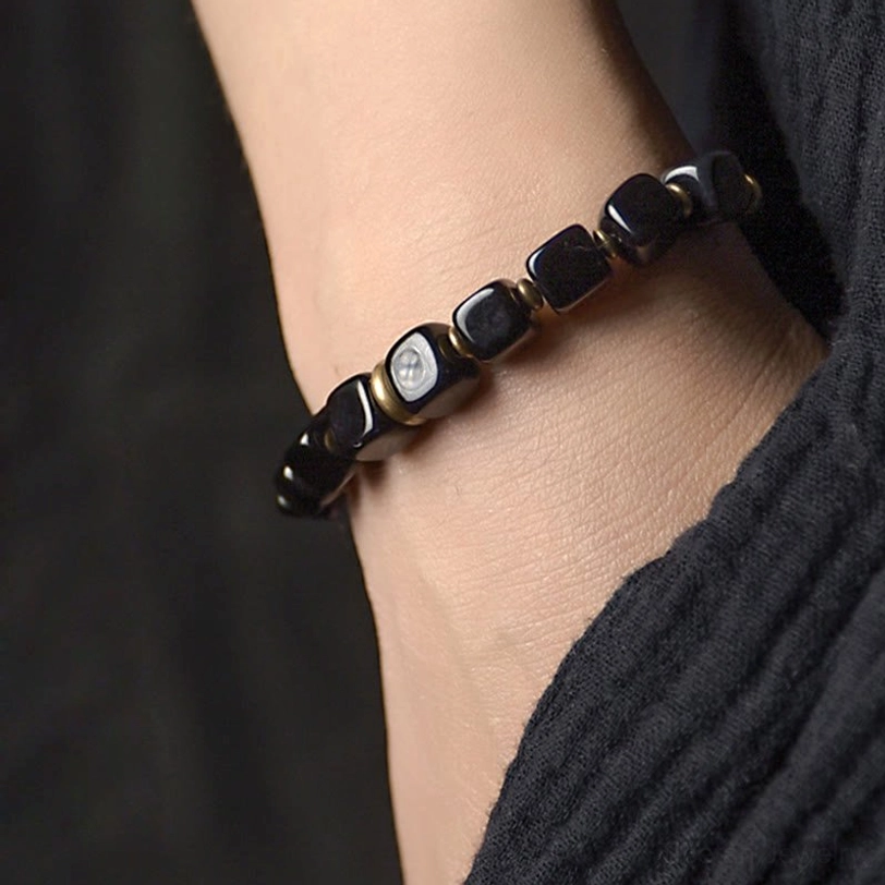 Black obsidian couple bracelet worn on wrist with dark fabric, close-up side view showing stone bead detail and comfortable fit